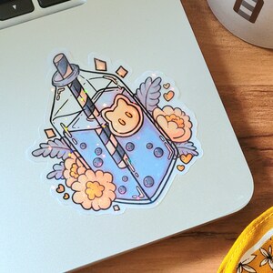 May include: A sticker of a clear glass bottle with a blue drink and boba pearls, a straw, and a cute bear face on the bottle. The bottle is surrounded by flowers and hearts.