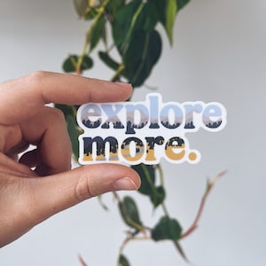 May include: A white sticker with the words "explore more." in a stylized font. The word "explore" is in light blue with a mountain and tree design. The word "more" is in black and gold.