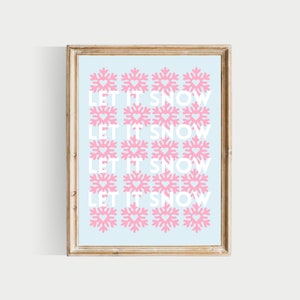 May include: A framed print with a light blue background and a repeating pattern of pink snowflakes with hearts in the centre. The text "LET IT SNOW" is repeated four times in white.