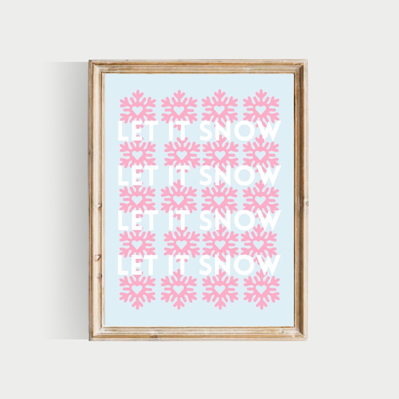 May include: A framed print with a light blue background and a repeating pattern of pink snowflakes with hearts in the centre. The text "LET IT SNOW" is repeated four times in white.