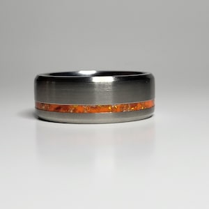 May include: A silver ring with a thin orange band. The band has a speckled pattern.