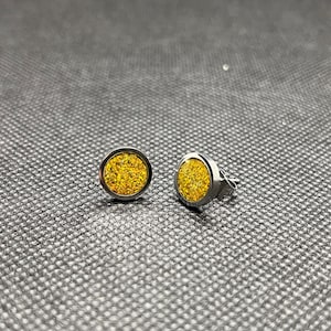 Puede incluir: Un par de pendientes de botón plateados con un diseño redondo de purpurina amarilla.