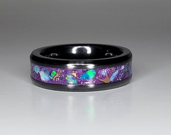 May include: A black ring with a purple and iridescent inlay. The inlay is made of small pieces of opal and other gemstones.