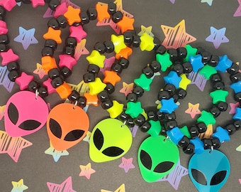 May include: Four neon colored friendship bracelets with black beads and star-shaped charms. Each bracelet has a neon alien charm attached.