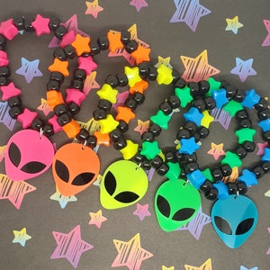 May include: Four neon colored friendship bracelets with black beads and star-shaped charms. Each bracelet has a neon alien charm attached.
