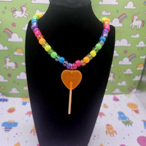 A neck model is wearing the orange lollipop necklace
