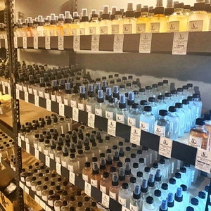 May include: A shelf unit filled with rows of small glass bottles with black lids and labels. The bottles are filled with a clear liquid and have labels with the text "Moon Water" and "Library".