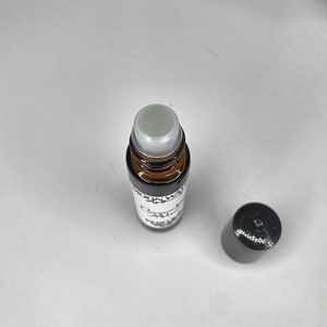Pode incluir: Um frasco de vidro castanho com um rolo, um r&oacute;tulo branco com a inscri&ccedil;&atilde;o "Moon Water" e "Omnia" em preto. O frasco tem uma tampa preta.