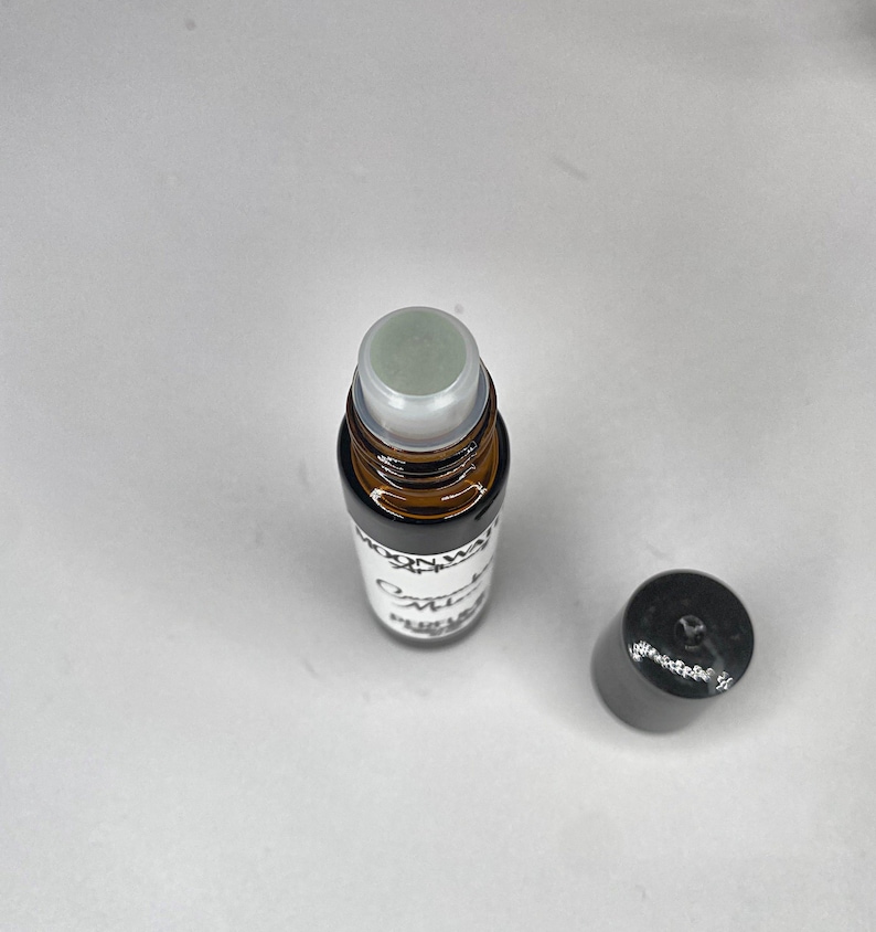Pode incluir: Um frasco de vidro castanho com um rolo, um r&oacute;tulo branco com a inscri&ccedil;&atilde;o "Moon Water" e "Omnia" em preto. O frasco tem uma tampa preta.