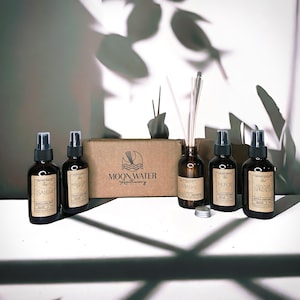 May include: Five brown glass bottles with labels and spray tops, a brown box with the text "MOONWATER Apothecary", and a glass bottle with a diffuser stick in a box. The bottles are labeled "SALEM", "MASQUE OF", "CITHAKE", "NEROLI", and "SILVER SPRINGS".