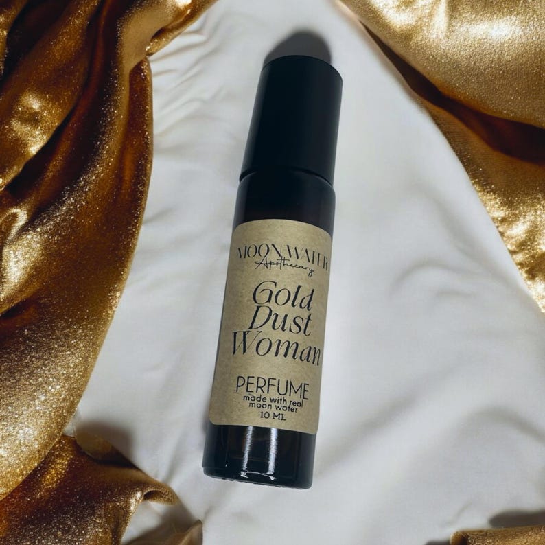 Pode incluir: Um pequeno frasco de vidro castanho com uma tampa preta e um r&oacute;tulo que diz "Moonwater Apothecary Gold Dust Woman Perfume made with real moon water 10 ml".