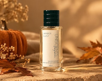 Könnte beinhalten: Ein durchsichtiger Glasparfümflakon mit einem dunkelgrünen Verschluss und einem weißen Etikett mit der Aufschrift AMBER LUST UNISCENTS fragrance EAU DE PARFUM Amber | Musk | Black Pepper | Sandalwood | Vanilla 2 fl oz. Der Flakon ist rechteckig geformt.