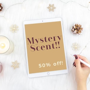 May include: A white tablet with a brown background displaying the text "Mystery Scent!! 50% off!"  The tablet is on a white fuzzy surface with decorative snowflakes and pine cones.