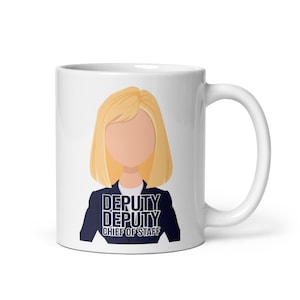 Puede incluir: Taza de cerámica blanca con una ilustración de dibujos animados de una mujer con cabello rubio y una chaqueta azul. El texto "DEPUTY DEPUTY CHIEF OF STAFF" está impreso debajo de la ilustración.