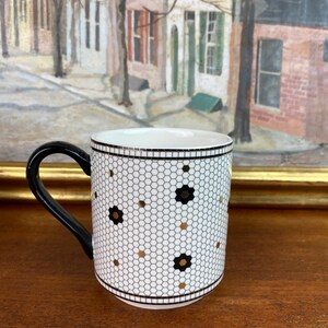 May include: White ceramic mug with a black handle. The mug has a black and gold geometric pattern that resembles a honeycomb.