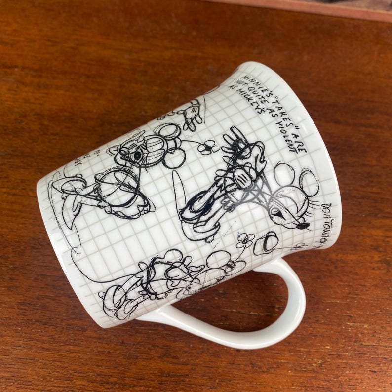 Puede incluir: Taza de cer&aacute;mica blanca con bocetos en blanco y negro de Mickey y Minnie Mouse sobre un fondo de cuadr&iacute;cula. La taza tiene un asa curva y el texto "Minnie's takes are not quite as violent as Mickey's".