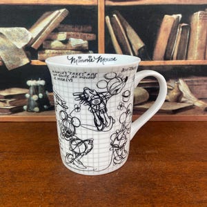 Puede incluir: Taza de cer&aacute;mica blanca con bocetos negros de Minnie y Mickey Mouse. La taza tiene las palabras "Minnie Mouse" y una cita. La taza tiene un asa curva y est&aacute; decorada con un patr&oacute;n de cuadr&iacute;cula.