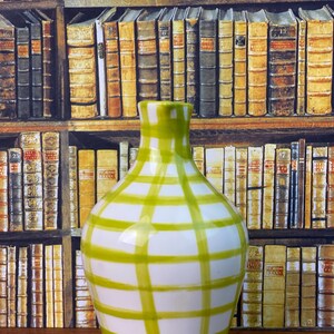 May include: A white ceramic vase with a green grid pattern. The vase has a rounded body and a narrow neck. The background shows a wallpaper design of bookshelves filled with books.
