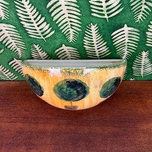 May include: A semi-circular ceramic wall planter featuring a hand-painted design of dark green circular tree motifs against a textured yellow and orange background. The upper rim has a mottled green border, and the flat back is designed for mounting.