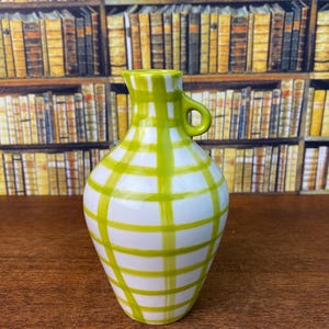 May include: A white ceramic jug with a green plaid pattern. The jug features a small handle and a spout. The green plaid design covers the body of the jug, creating a decorative and eye-catching look. The jug is likely used for serving beverages.