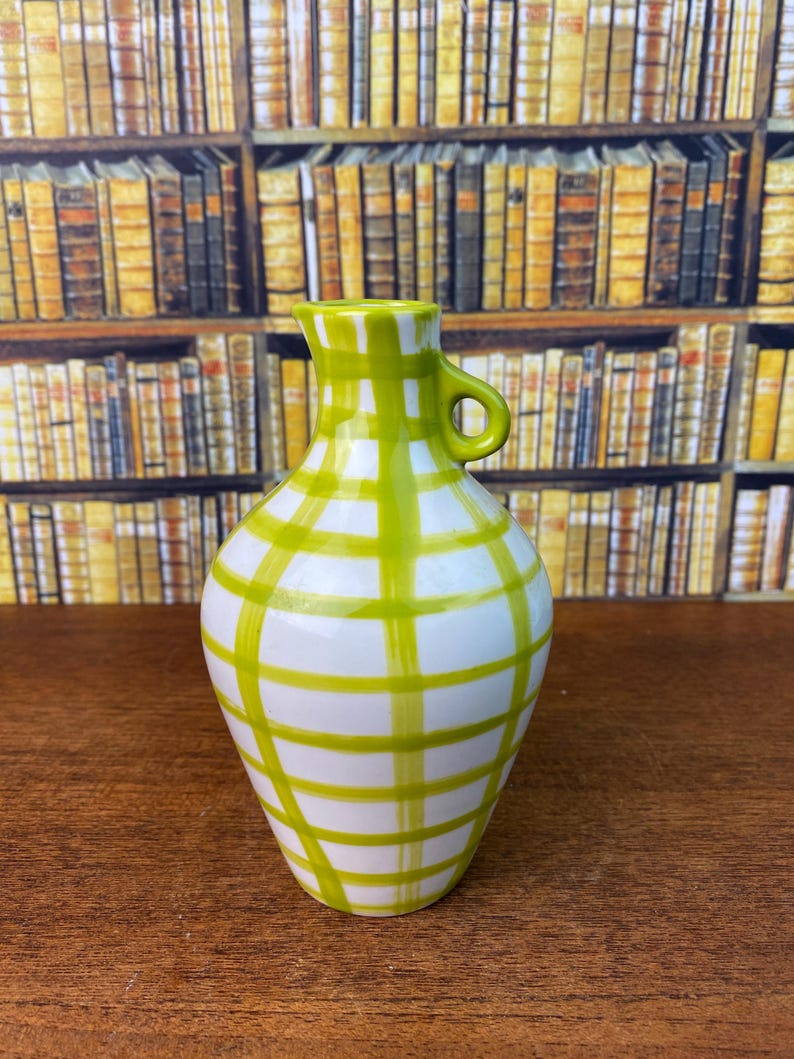 May include: A white ceramic jug with a green plaid pattern. The jug features a small handle and a spout. The green plaid design covers the body of the jug, creating a decorative and eye-catching look. The jug is likely used for serving beverages.