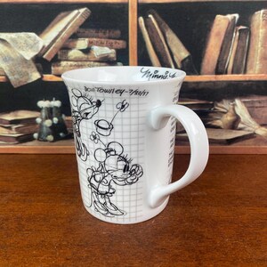 Puede incluir: Taza de cer&aacute;mica blanca con un boceto en blanco y negro de Minnie Mouse sobre un fondo de cuadr&iacute;cula. La taza tiene un asa curva y el texto "Don Towsley - 7/20/57" y "Minnie". Un coleccionable encantador para los fans de Disney.