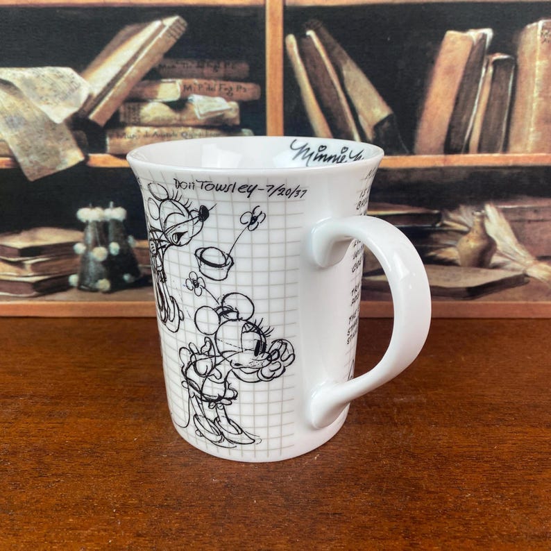 Puede incluir: Taza de cer&aacute;mica blanca con un boceto en blanco y negro de Minnie Mouse sobre un fondo de cuadr&iacute;cula. La taza tiene un asa curva y el texto "Don Towsley - 7/20/57" y "Minnie". Un coleccionable encantador para los fans de Disney.