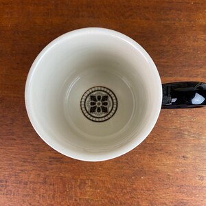May include: White ceramic mug with a black handle. The inside of the mug has a black and white geometric design.