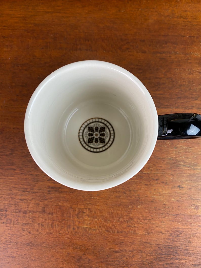 May include: White ceramic mug with a black handle. The inside of the mug has a black and white geometric design.