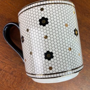 May include: White ceramic mug with a black and gold honeycomb pattern. The mug has a black handle.