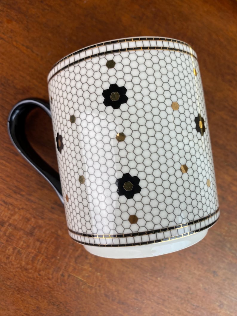 May include: White ceramic mug with a black and gold honeycomb pattern. The mug has a black handle.