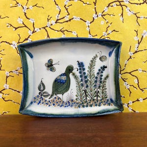 May include: A rectangular ceramic tray with curved sides featuring a hand-painted green bird, blue and green floral sprigs, and two butterflies. The tray has a white center with a speckled base and a dark blue and green gradient border.