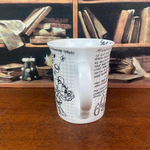 Puede incluir: Taza de cer&aacute;mica blanca con un dise&ntilde;o de boceto de Minnie Mouse en blanco y negro. La taza tiene un asa y texto que dice "Minnie is of the basic..." y "Towsley-7/20/37". La taza est&aacute; sobre una superficie de madera.