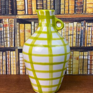 May include: White ceramic jug with a green plaid pattern. The jug has a handle and a spout. The green plaid design covers the white surface of the jug. The jug is a decorative item.