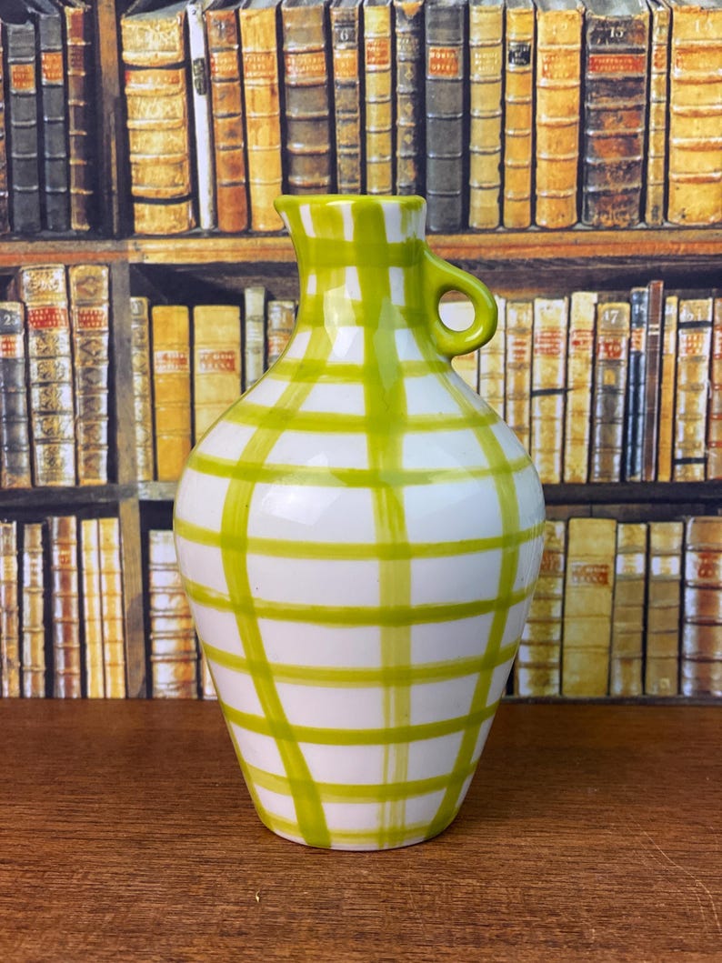 May include: White ceramic jug with a green plaid pattern. The jug has a handle and a spout. The green plaid design covers the white surface of the jug. The jug is a decorative item.