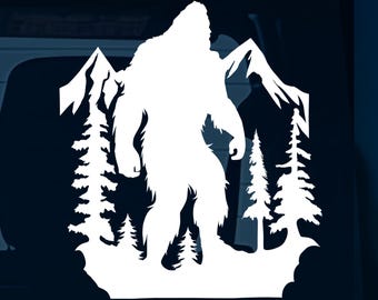 May include: White vinyl decal of a Bigfoot standing in a forest. The decal is on a dark blue car window.
