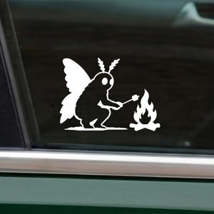 May include: A white vinyl decal applied to a car window featuring a stylized moth character with antennae and wings, sitting in a crouched position while holding a stick over a small campfire to roast a marshmallow, rendered in a solid silhouette.