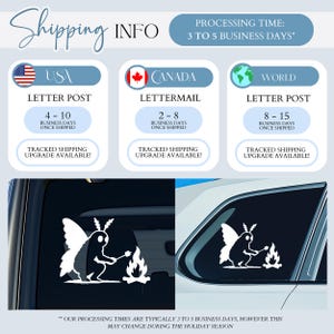 May include: A white vinyl decal featuring a moth-like creature with wings sitting by a campfire and roasting a marshmallow on a stick. The design is shown applied to the rear window of a vehicle, displaying a clear silhouette against the dark glass.