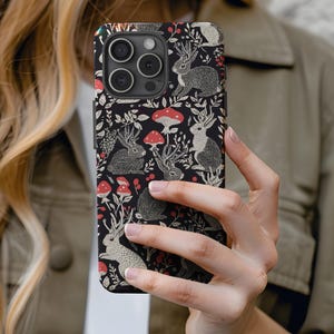 May include: A black phone case with a repeating pattern of white rabbits, red mushrooms, and green leaves.