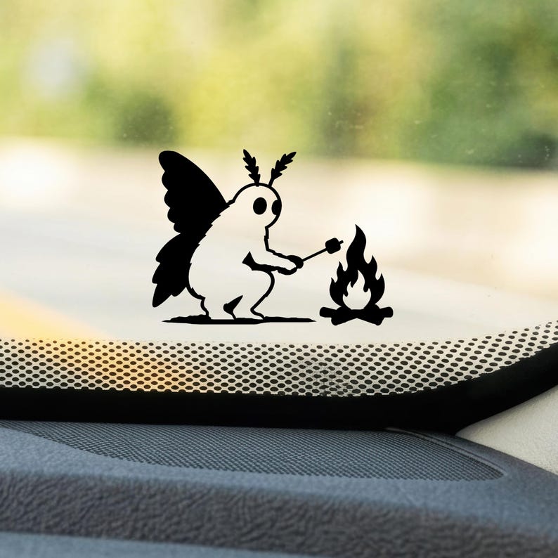 May include: A black and white vinyl decal featuring a moth-like creature with large wings and antennae, sitting and holding a stick over a small campfire. The design is rendered in a solid, high-contrast graphic style on a transparent background.
