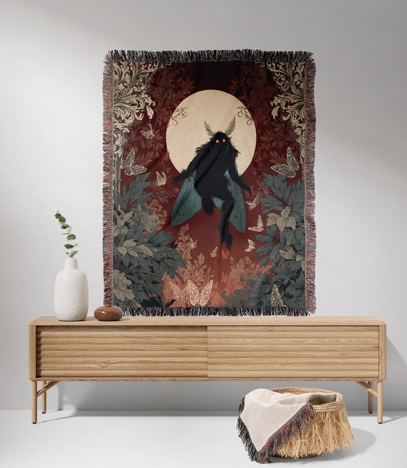 May include: A woven tapestry featuring a dark figure with moth-like wings against a backdrop of a full moon and foliage. The tapestry has a fringed edge and is displayed on a light wood cabinet. Butterflies and floral patterns are also visible.