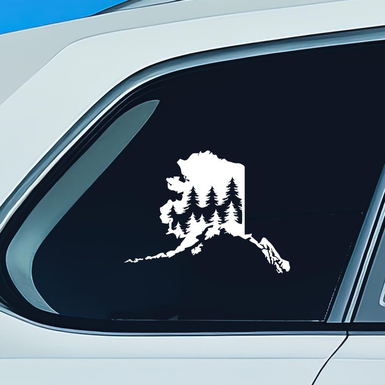 May include: A white vinyl decal applied to a car window, featuring the silhouette of the state of Alaska filled with a detailed graphic of a dense evergreen forest. The design shows multiple rows of pine trees within the state border outline.