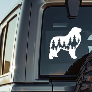 May include: White silhouette of a Bernese Mountain Dog with a forest scene inside the silhouette. The dog is standing on all four legs with its head facing to the right. The image is on a black car window.