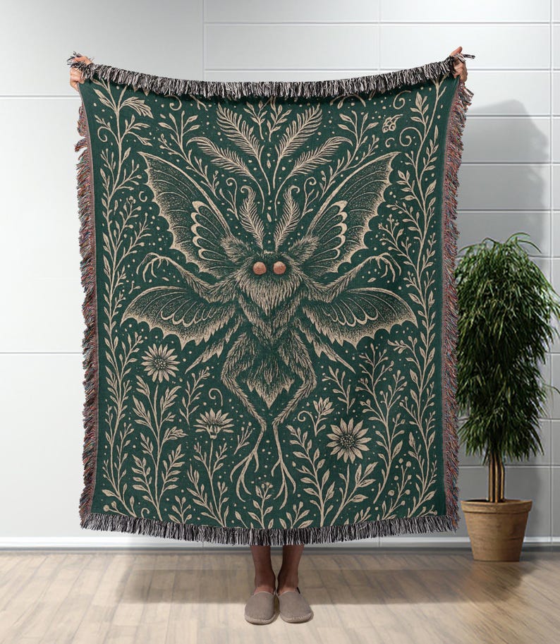 Puede incluir: Una manta verde oscuro con un dise&ntilde;o detallado de polilla y flores. La polilla es beige con alas grandes y un cuerpo peludo. Patrones florales y de hojas beige rodean la polilla. La manta tiene un borde con flecos.