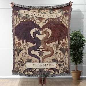 Peut inclure: Une couverture tissée avec un motif de deux dragons formant un cœur. Les dragons sont dans des tons violets et bruns, sur un fond beige avec des motifs floraux. Le texte "Eternally Yours" et "Lexie & Mark" est affiché sur la couverture.