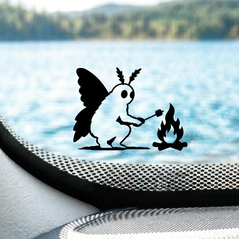 May include: A black vinyl decal featuring a moth-like creature with large wings and antennae, sitting and roasting a marshmallow on a stick over a small campfire. The design is solid black and is applied to a transparent surface.