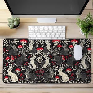 May include: Black mouse pad with a repeating pattern of white rabbits with antlers, red mushrooms, and white berries on a black background.