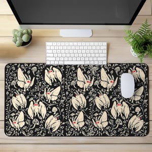 May include: Black and white mouse pad with a repeating pattern of moths and flowers. The moths have red eyes and are flying in a variety of directions. The flowers are white and have a simple design.