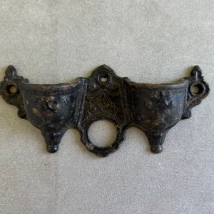 May include: A black cast iron wall mounted holder with three small cups. The holder has a decorative design with a floral motif.