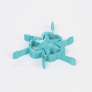 Pu&ograve; includere: Oggetto turchese stampato in 3D con una stella al centro, circondato da un design circolare con bracci rettangolari. L'oggetto &egrave; probabilmente decorativo o un componente di un design pi&ugrave; ampio. Misure in centimetri.